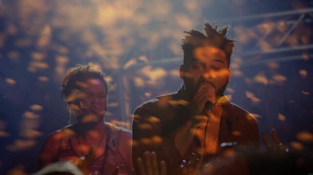 Lead singer raising mic singing to move music crowd at concert, golden confetti drifting over faces