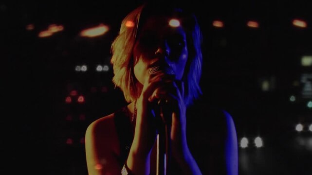 Woman singer lowering hands, bringing mouth to mic, singing music while bokeh drifting across watch