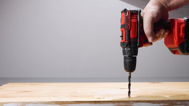 The cordless drill lowers the bit into the pine board and drills a clean hole. A close-up of the workshop: sawdust, wood grain and steady hands.