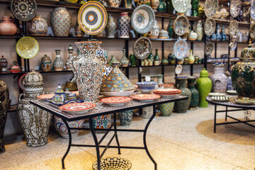 Colorful ceramic pottery displayed on a table in a vibrant market, showcasing intricate designs and patterns, surrounded by various decorative items and cultural artifacts