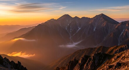 Naklejka premium Golden light bathes the rugged peaks of a mountain range at sunset