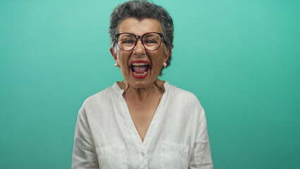 Senior woman with grey hair in glasses and white blouse expresses various emotions against a green...