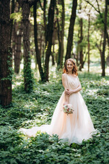 Fototapeta premium Blonde bride in a light coral dress in a green forest