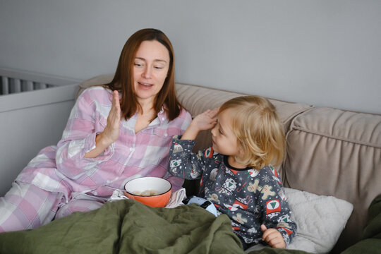 Mother and son having breakfast or snack in bed together in pajamas, family bonding moment while eating breakfast in cozy bedroom with pillows - Powered by Adobe