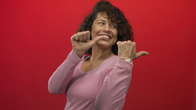 Hispanic woman wearing pink shirt pointing thumb to chest in studio; confidence empowerment positivity. - Powered by Adobe