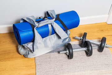 Gym bag with blue pilates or yoga mat and metal dumbbells in the hallway waiting to go to a class, health and fitness concept