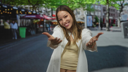 Fototapeta premium Young hispanic woman smiling with hands to chest, wearing white shirt and yellow tank on street; gratitude warmth connection.