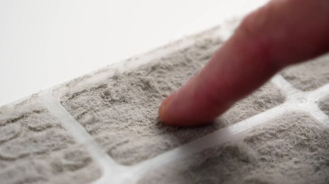 Dirty air conditioner filter panel and finger scraping off dust fibers on white table. Macro shot