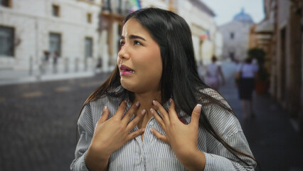 Young woman expressing emotion in a historic old town street during daytime with blurred buildings in the background, showcasing urban and cultural ambiance.