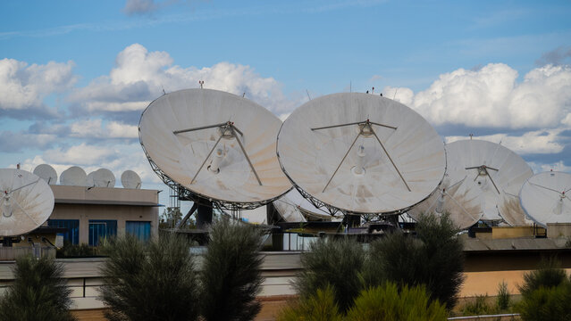 Satellite dishes at a telecommunications facility with clouds and industrial structures