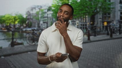 Man tapping smartphone with hands visible on cobblestone street by amsterdam canal bridge; concentration connection.