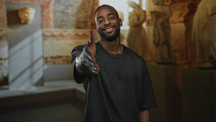 Man smiling extends hand for handshake in museum gallery among sculptures and pedestals; warmth greeting.