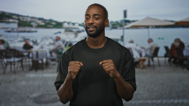 Young african american man with clenched fists celebrating on a restaurant terrace by the waterfront; celebration joy.
