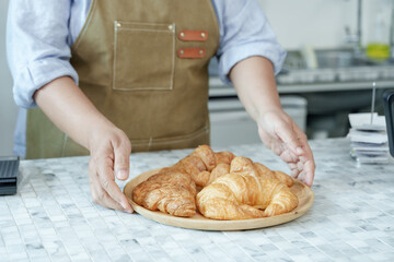 Asian barista placing plate of croissants on marble counter, showcasing pride, precision, dedication to quality service, symbolizing warmth and authenticity of small bakery cafe.