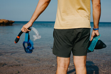 Man holds flippers and diving mask against the sea.