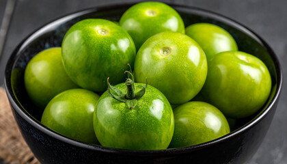 Fresh green tomatoes in dark ceramic bowl, vibrant and organic, natural food product. Tasty vegetable.