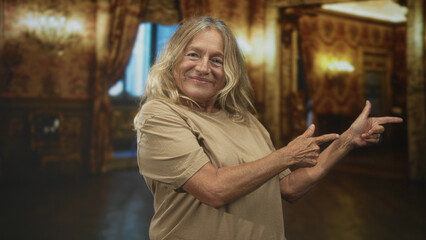 Senior woman pointing fingers with bare hands, smiling in an ornate ballroom building; contentment acceptance.