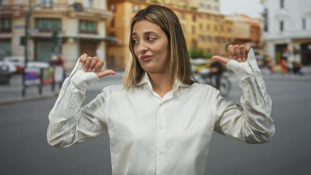 Woman pointing both thumbs to her chest on a busy street with blurred city buildings and cars in view; smug defiance.