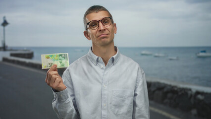 Man holding israeli shekel banknote by the seaside near a port, capturing outdoor financial themes...