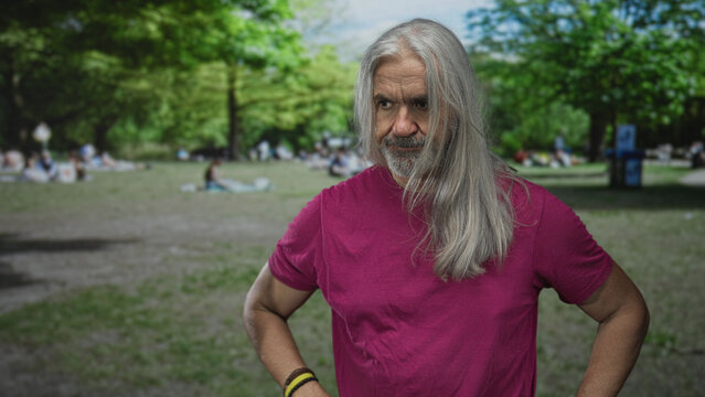 Man covering mouth with hand in forest park with long gray hair, wearing pink shirt; concern reflection. - Powered by Adobe