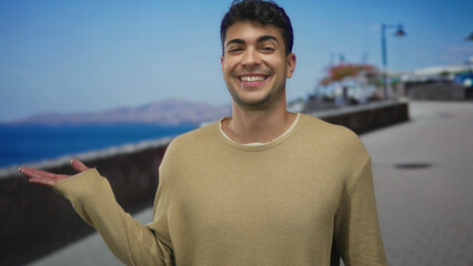 Man raises hand while presenting a seaside walkway view that hispanic guy enjoys outdoor scenery,...