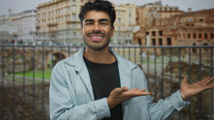 Man extends palms to each side in front of sunlit ancient building with roman ruins outdoors;...