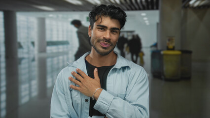 Obraz premium Young hispanic man smiles revealing white teeth in a spacious bright airport terminal; friendly greeting.