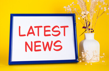 Latest News symbol. Concept words Latest News on beautiful wooden picture frame. Beautiful yellow background with flower vase. Business and Latest News concept. Copy space.