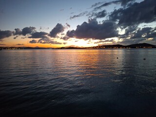 Dramatic sunset over the sea captured during the golden hour or twilight. Intense red, orange, and gold colors illuminate the sky and are strongly reflected on the dark, rippled water below.