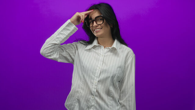 Woman wearing glasses and pointing finger while smiling against vibrant purple studio setting; confidence.