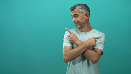 Middle age man with grey hair, crossed arms pointing index fingers left and right in teal studio; playful choice.