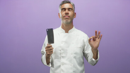 Chef in white jacket holds cleaver and makes ok hand gesture while looking upward in studio; confidence craft.