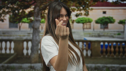 Woman smiling on street making money gesture outdoors suggesting happiness and confidence in city environment under sunny sky with trees background.