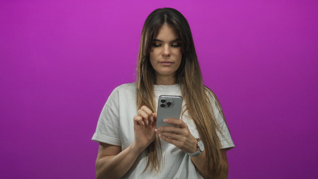 Woman using smartphone over isolated purple background, expressing focus and engagement with device, showcasing modern technology and digital connectivity, dressed casually with long hair.