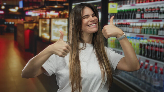 Woman smiling gives thumbs up in a vibrant indoor cafe, showcasing happiness and positivity with a background of colorful bottles and a warm restaurant ambiance.