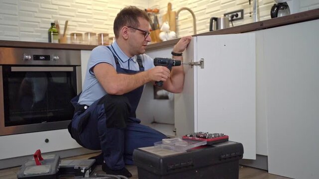 Handyman using an electric drill to install a kitchen cabinet door hinge