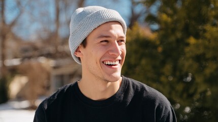 Man smiling in winter, wearing a knit cap and sunglasses, standing outdoors during daytime with clear sky.