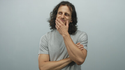 Young hispanic man with long hair hand on chin in studio with pale blue backdrop; thoughtful introspection reflection.