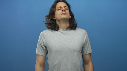 Man with eyes closed and head tilted back wearing grey t shirt in blue studio; serenity...