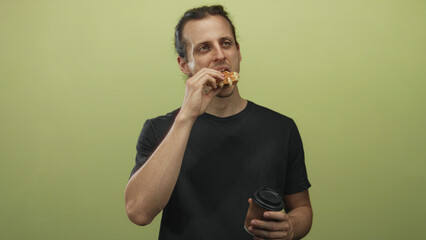 Man biting a waffle while holding a takeaway coffee cup in studio with light green wall; casual...