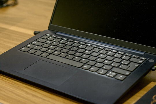 Primer plano angular de teclado de laptop negra sobre escritorio de madera. Tecnolog&iacute;a de oficina y trabajo remoto con distribuci&oacute;n de teclas en espa&ntilde;ol visible.