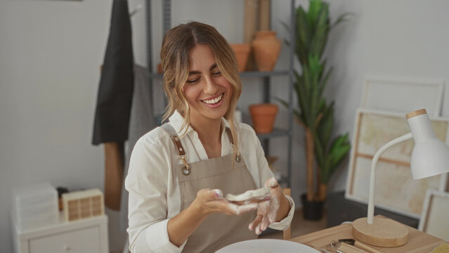 Young blonde woman holds fresh clay disc with bare hand in artisan pottery studio; joy creativity craftsmanship passion.