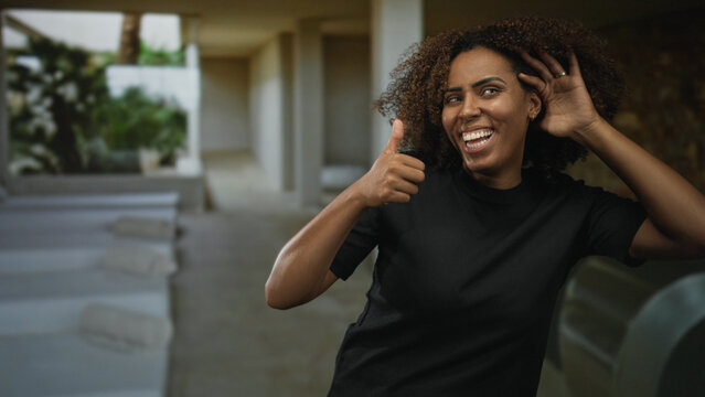 Woman giving thumbs up and holding hand to ear in a spa building poolside lounge; happiness relaxation wellness.