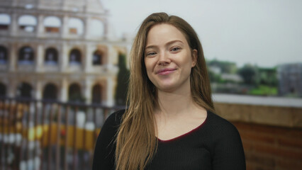 Fototapeta premium Young caucasian woman smiling with visible face and long hair at roman coliseum building on outdoor terrace under daylight; serenity.