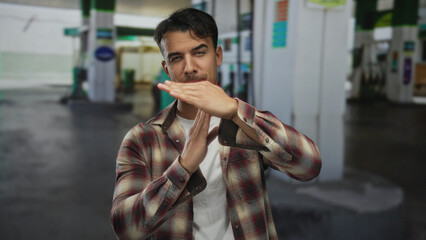 Young hispanic man making time-out gesture at a petrol station outdoor, wearing plaid shirt and...