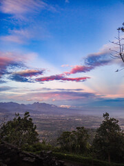 The view during a morning hike or sunrise on Mount Penanggungan is beautiful. It offers a vast landscape, including savannahs and ancient buildings like temples.