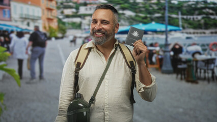 Man kissing passport while holding backpack strap and canteen on a street terrace near outdoor...