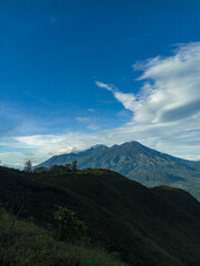 The view during a morning hike or sunrise on Mount Penanggungan is beautiful. It offers a vast landscape, including savannahs and ancient buildings like temples.
