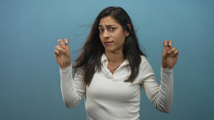 Woman displaying air quotes with both hands and raised eyebrows in blue studio setting; wry...
