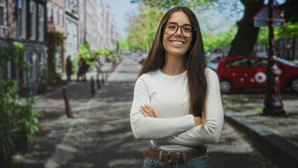 Woman giving thumbs up with visible thumb and smiling on a tree lined urban street by a red car and...